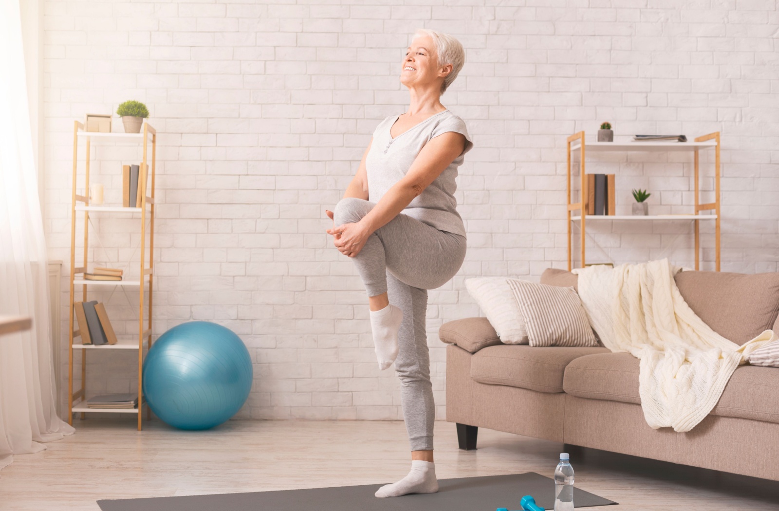 A senior woman standing on a yoga mat doing leg exercise